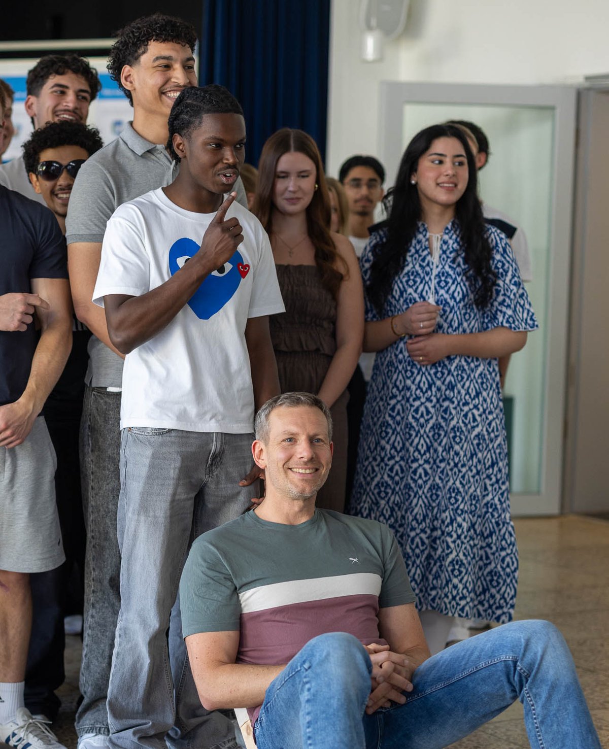 Lehrer sitzt lachend vor einer Gruppe Schüler:innen